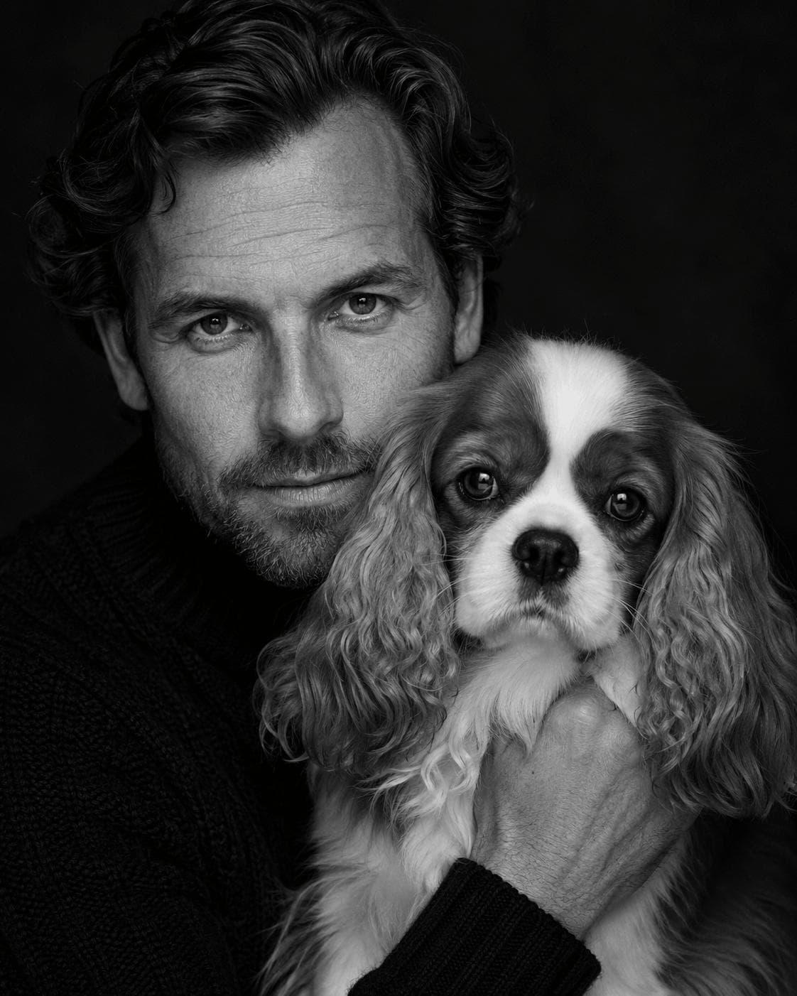 Black-and-white studio portrait of a person beside their king charles spaniel